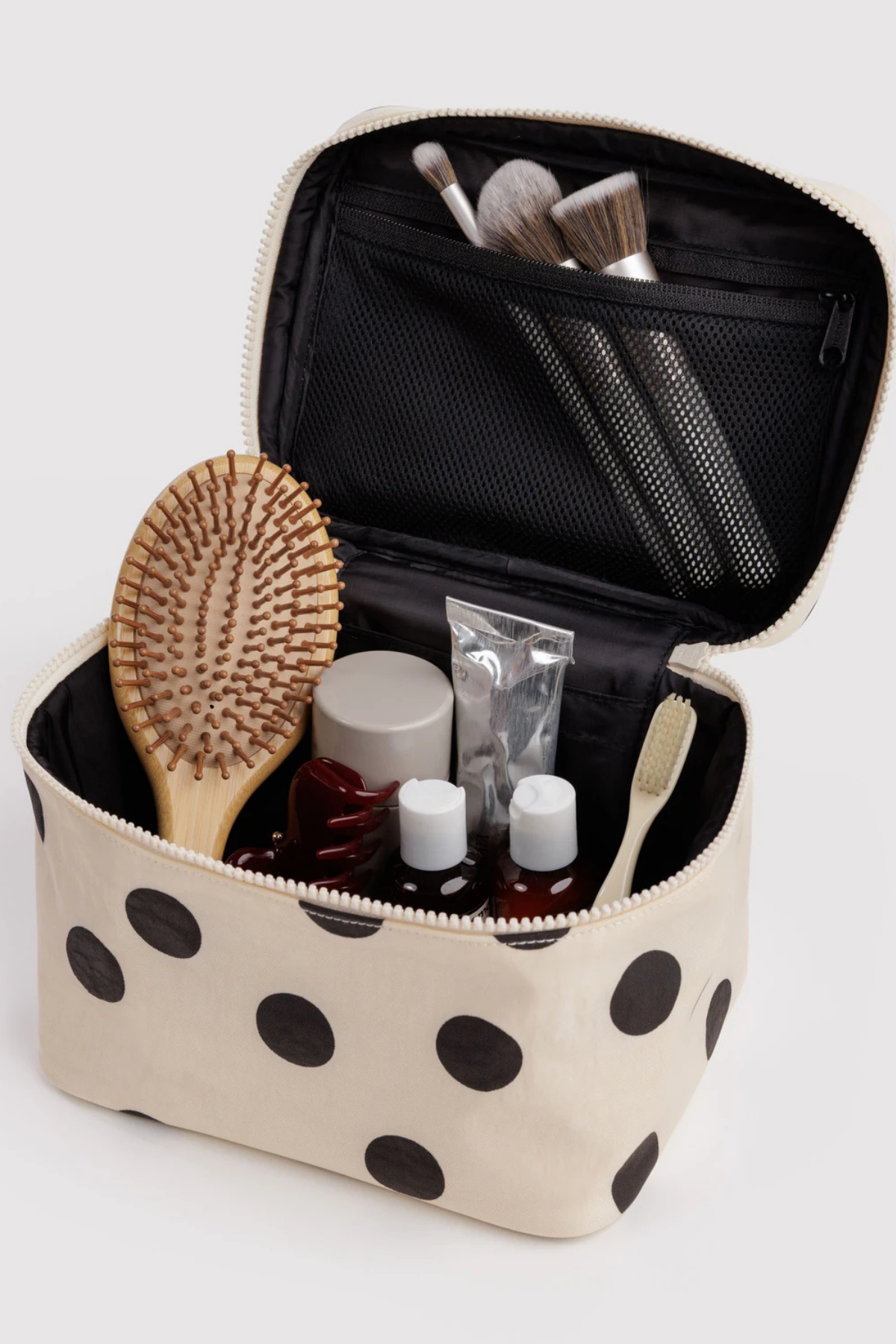 Open cream and black polka dot cosmetic case filled with brushes, hairbrush, and travel toiletries