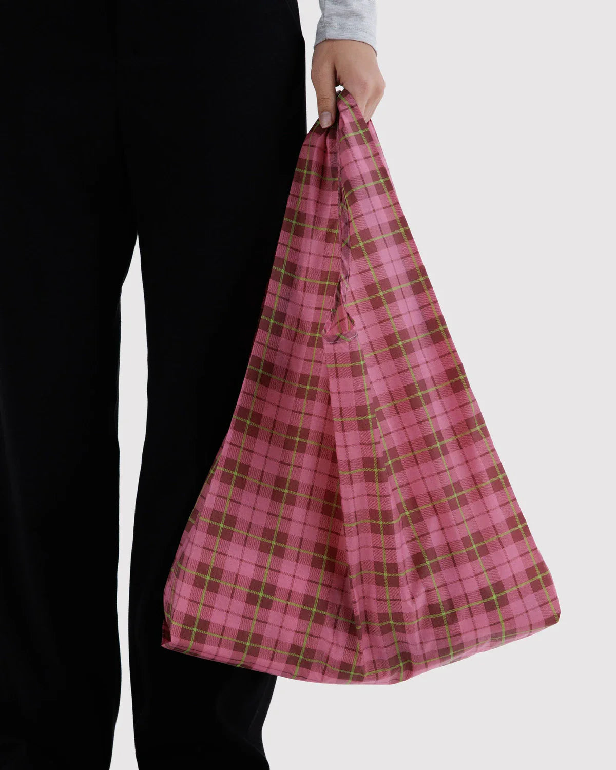 Model holding a pink tartan plaid reusable tote bag with dark red and lime green grid lines