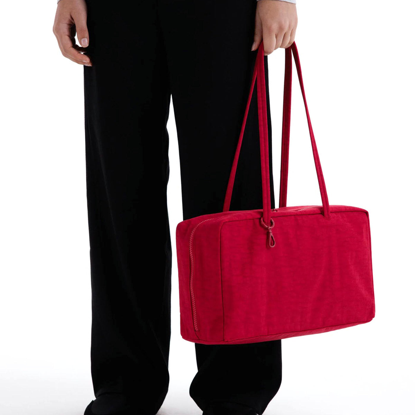 Model holding a cherry red medium nylon bowler bag with double top handles against white background