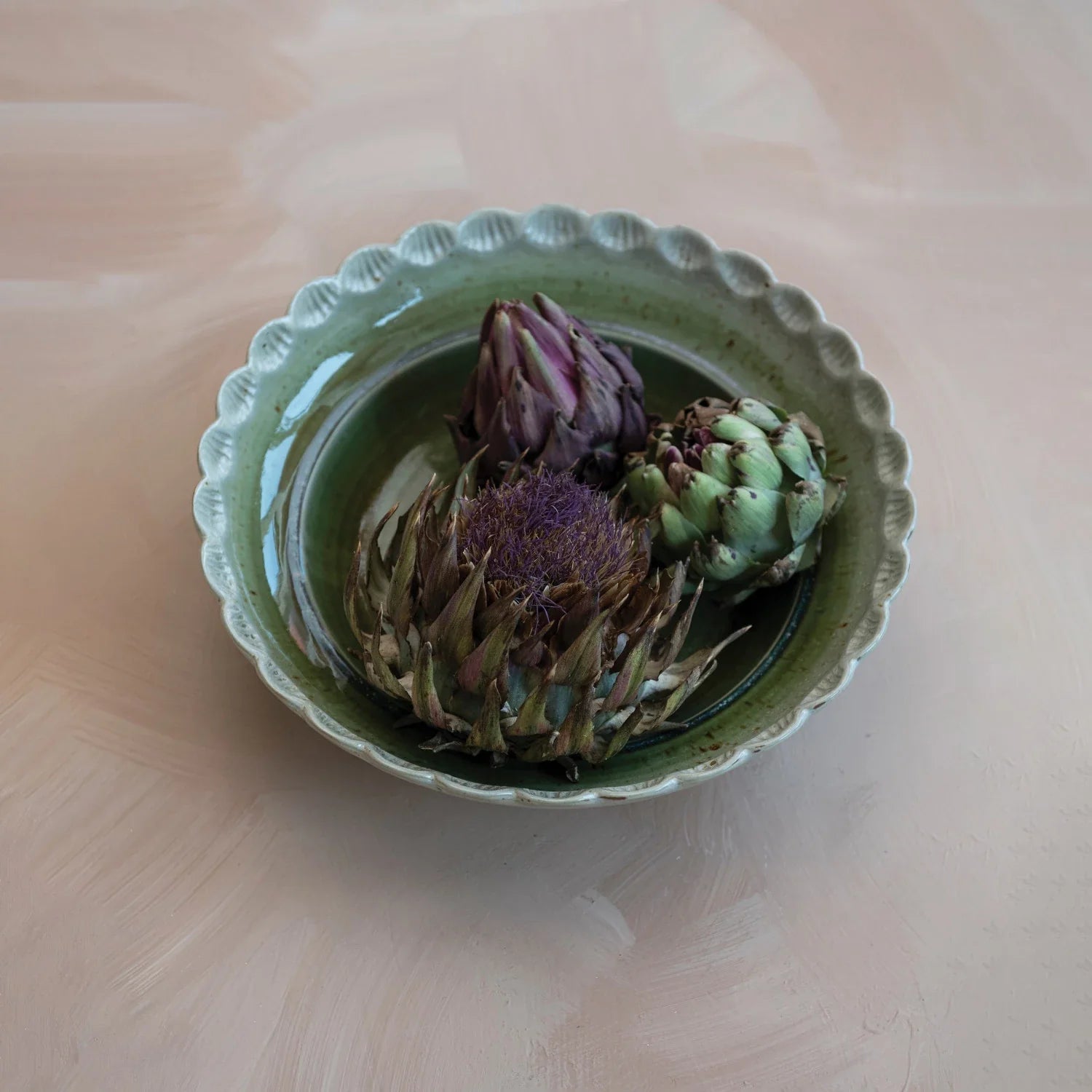Green ceramic scalloped bowl with artichokes displayed inside on wooden surface
