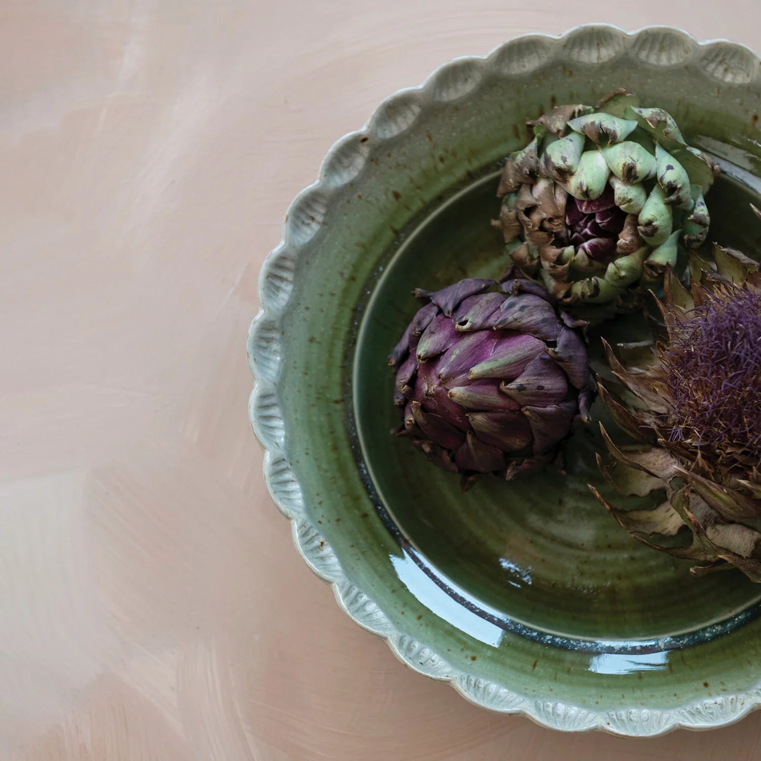 Green stoneware scalloped bowl with decorative artichokes on wooden surface
