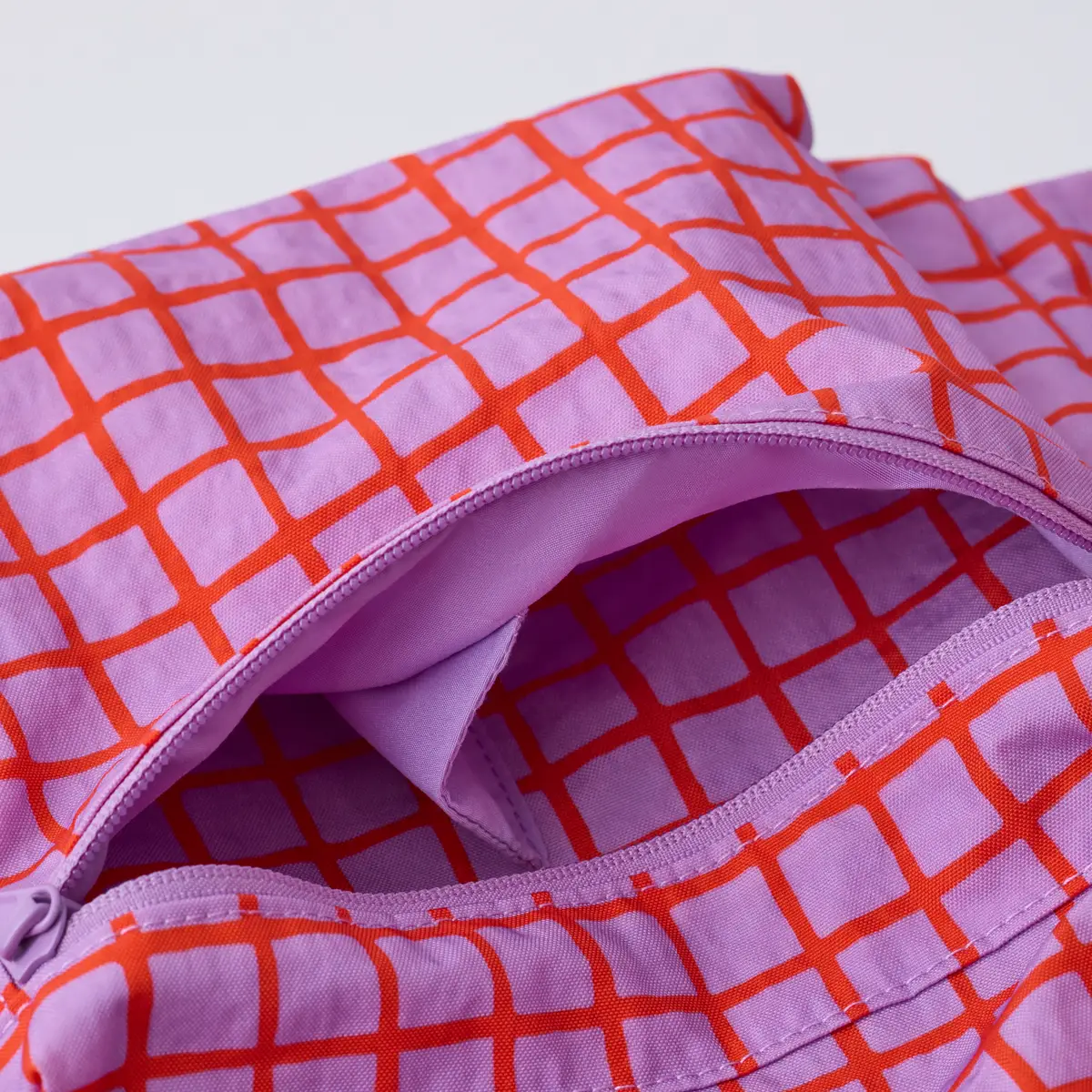 Close-up detail of purple backpack with red-orange grid pattern showing zipper and handle