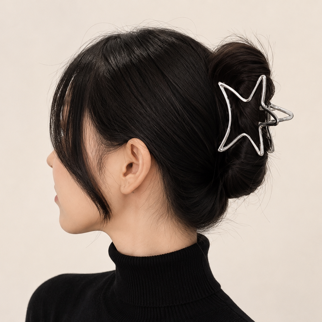 A woman shown in side profile wearing a black turtleneck sweater and a black hair claw clip with a silver outline star design, holding her hair in a low bun against a plain beige background.