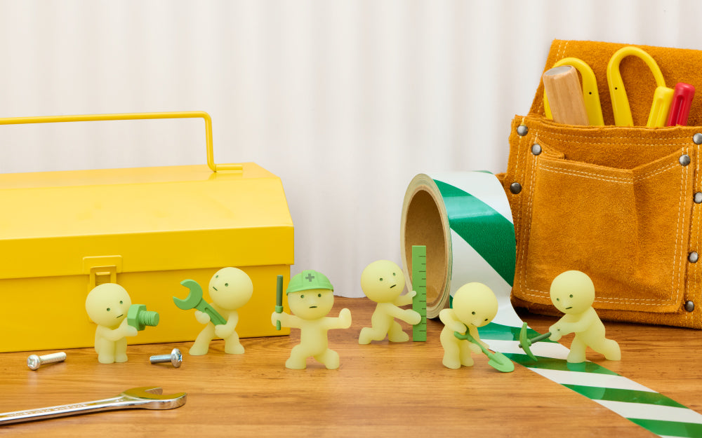 Six SMISKI construction minifigures holding tools near yellow toolbox and leather tool pouch