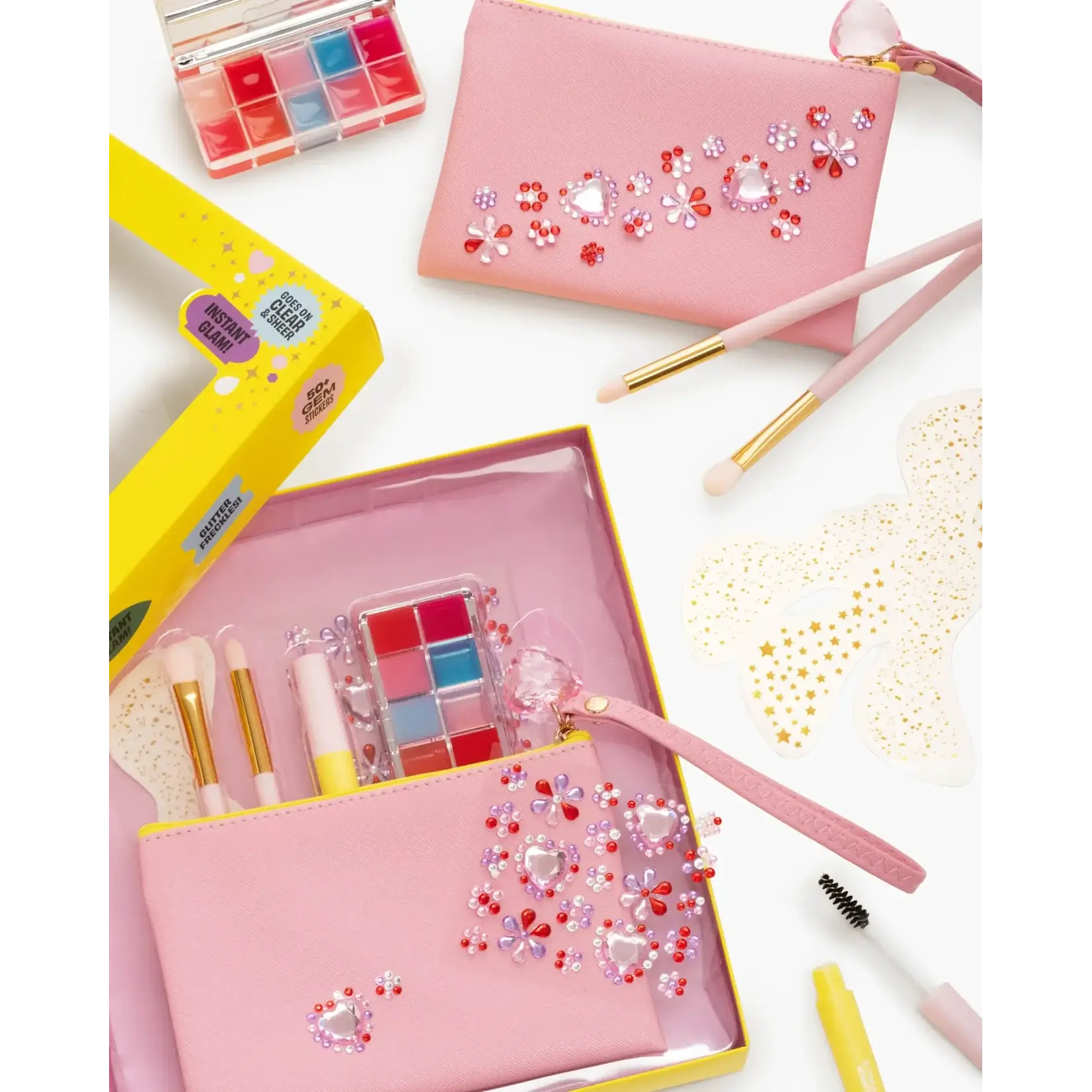 Pink makeup kit with eyeshadow palette, brushes, and decorative gems in yellow box